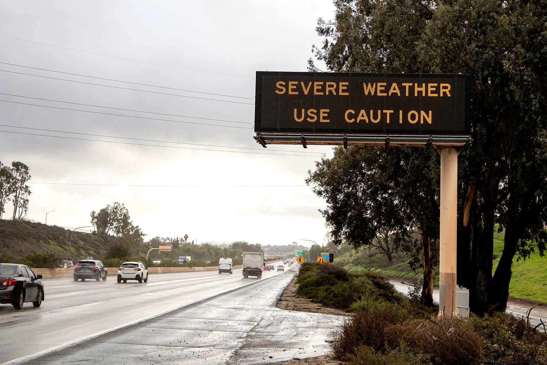 Digital sign at freeway stating Severe Weather Use Caution with wet freeway and traffic. The image is from the 15 freeway in San Diego County California